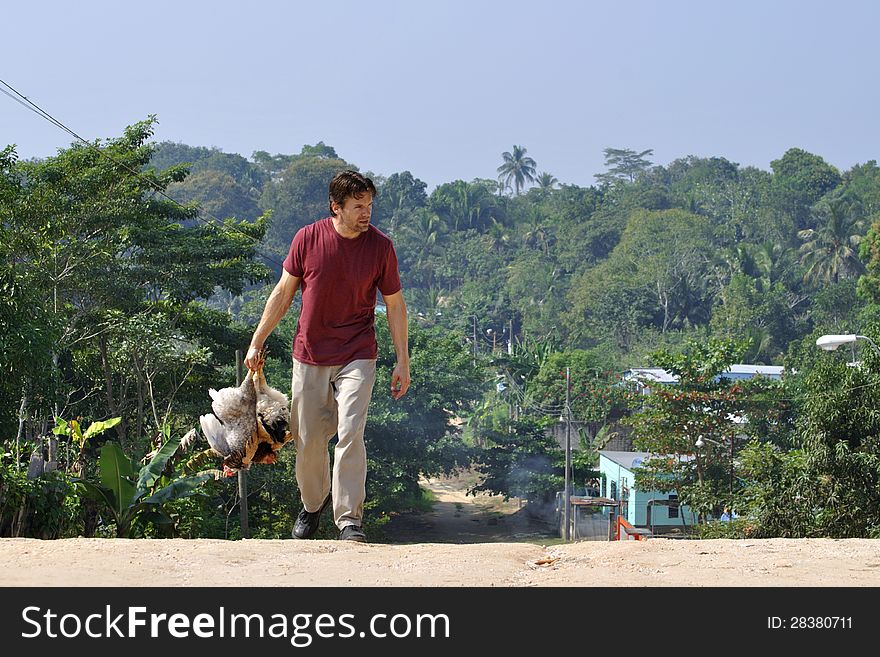 Caucasian man carries two chickens on dirt road in tropical village. Caucasian man carries two chickens on dirt road in tropical village