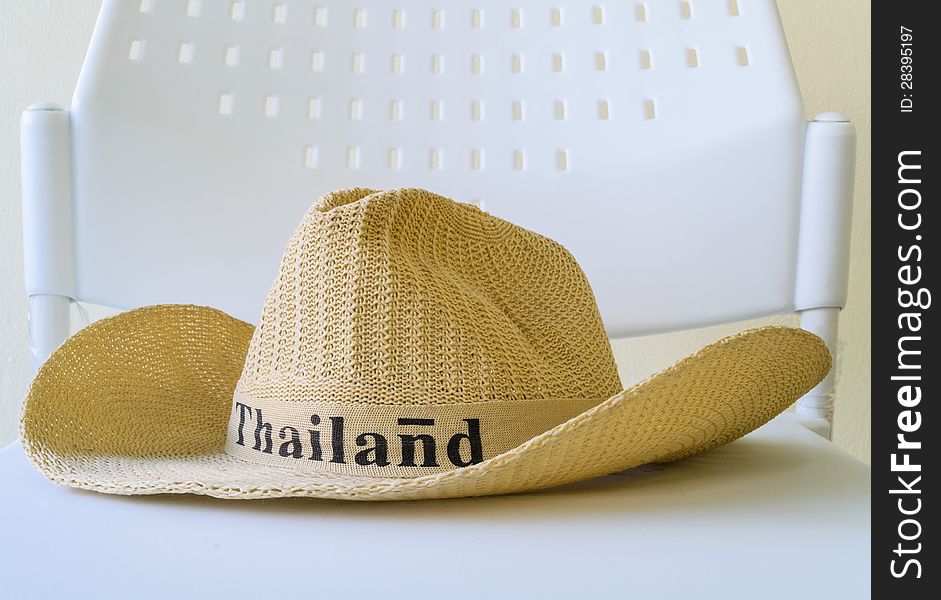 A hat with Thailand word is on a white chair. A hat with Thailand word is on a white chair
