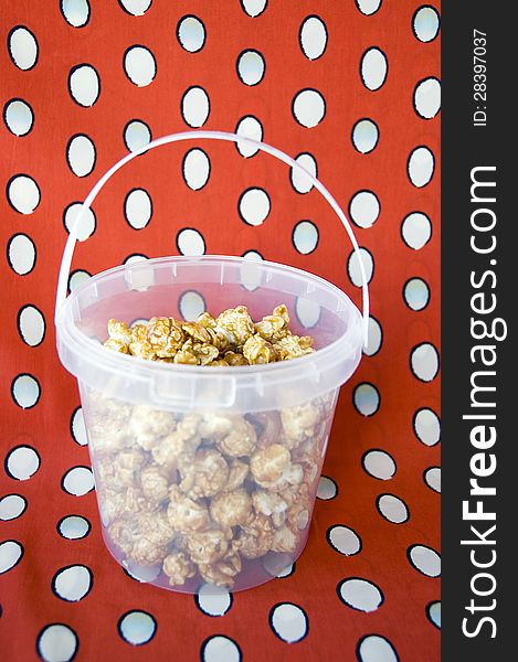 Caramel popcorn in plastic bucket on red background