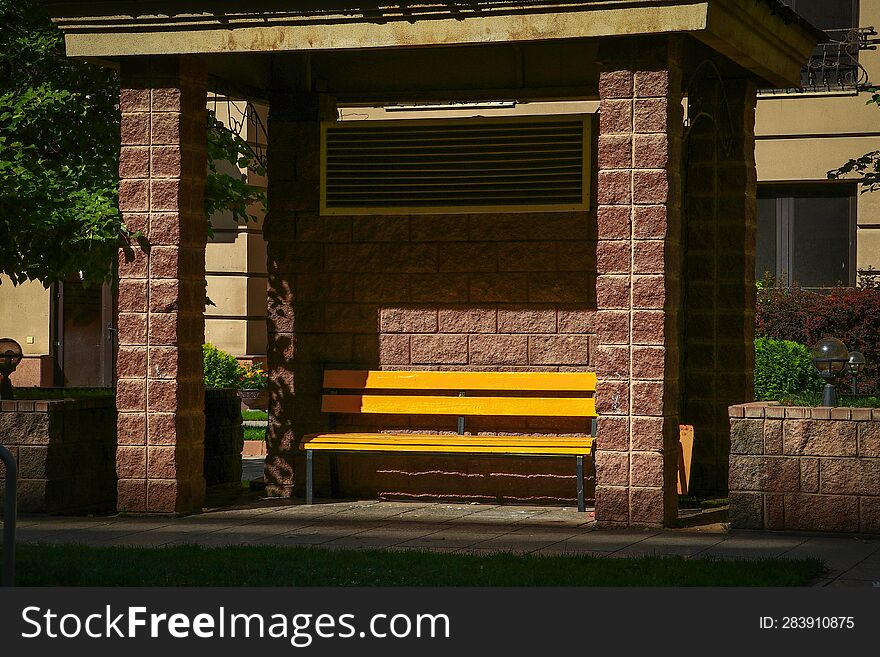 Yellow bench under a canopy in the courtyard of a residential building under the rays of the morning summer sun