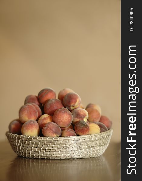 A basket overflowing with peaches, sitting on a wooden table in a rustic kitchen. A basket overflowing with peaches, sitting on a wooden table in a rustic kitchen