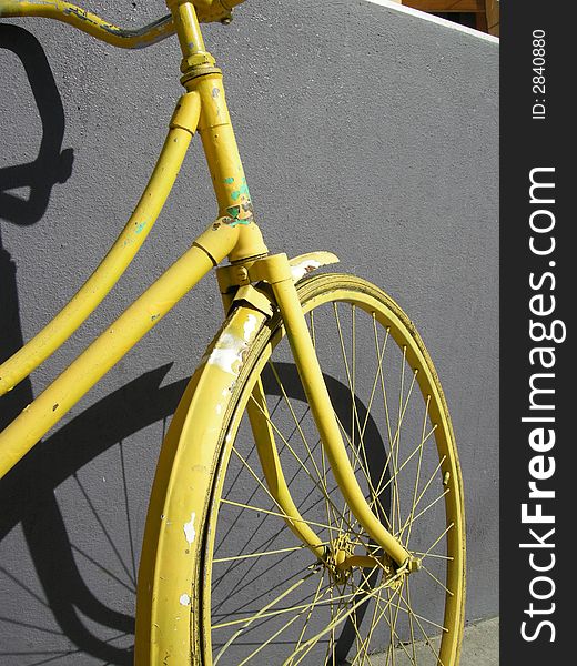 The front wheel of an old yellow bike leaning on a grey wall. The front wheel of an old yellow bike leaning on a grey wall