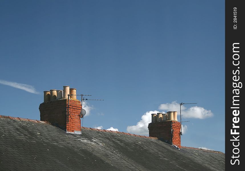 Red brick chimneys on terraced house roofs with blue sky and white clouds. Red brick chimneys on terraced house roofs with blue sky and white clouds