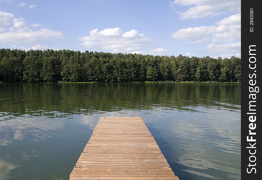 Wooden pontoon on a lake with forest opposite and blue sky above