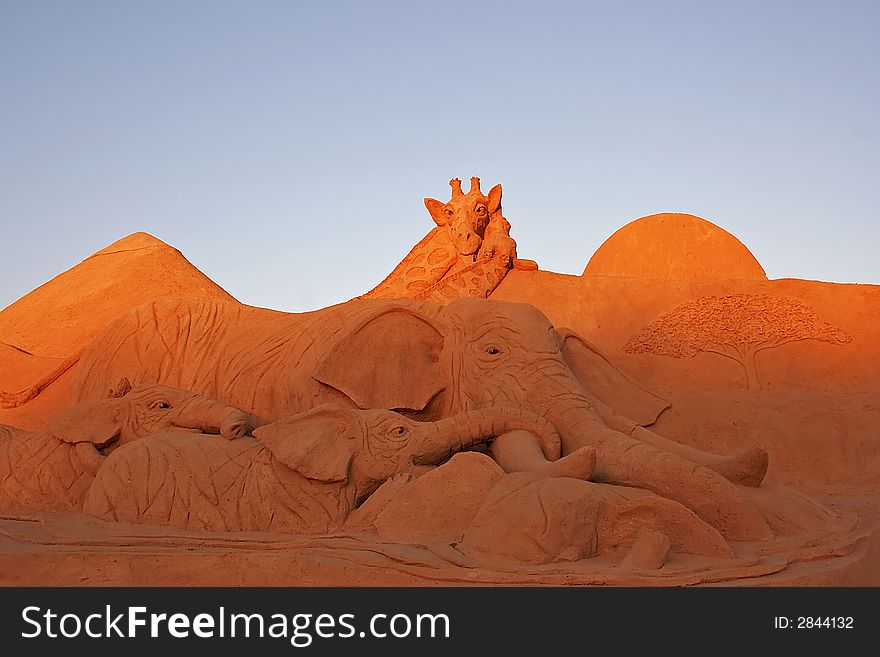 Giraffe and elephants in the desert made from sand against a blue sky