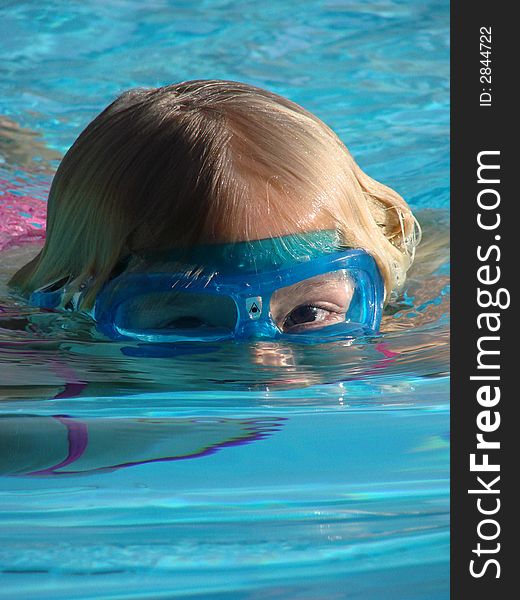 Young girl wearing goggles, with her face partially submerged in a swimming pool. Young girl wearing goggles, with her face partially submerged in a swimming pool.