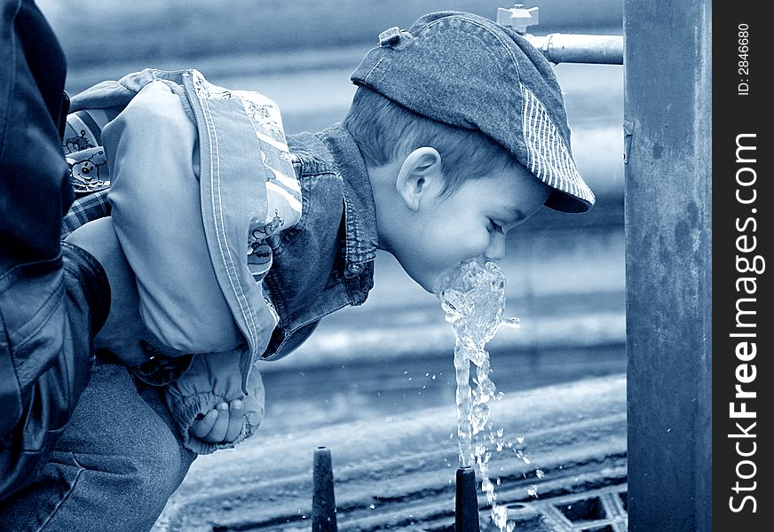 Little boy drinking water from a public fountain