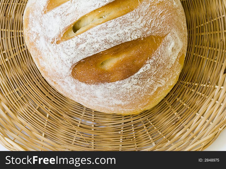 A round loaf of white bread on a woven plate (closeup)