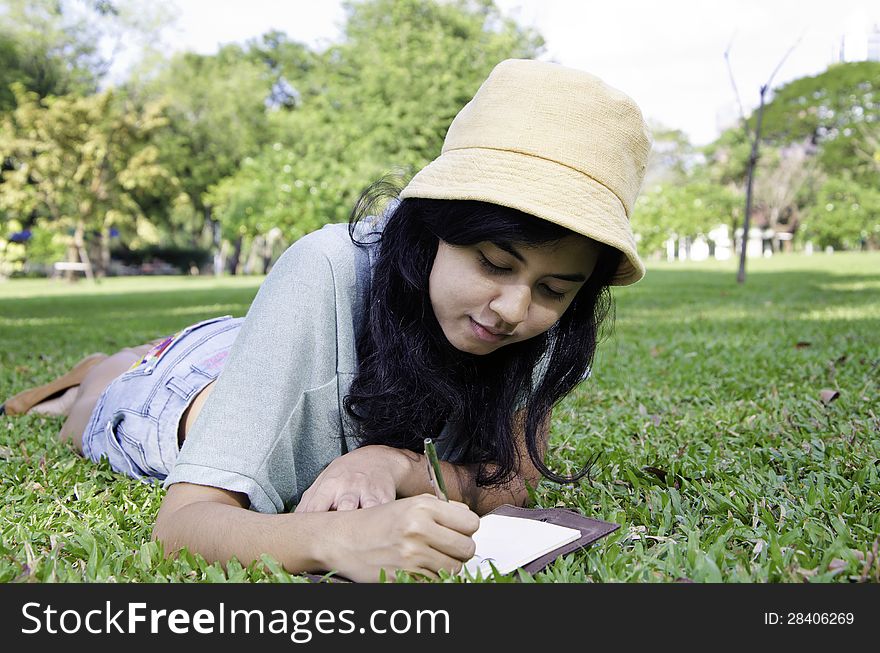 Beautiful teenage girl writting book, against green of summer park.