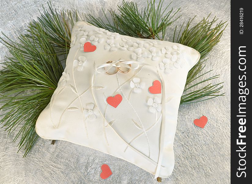 Wedding pillow with the golden rings, pine needles and hearts cut out of paper