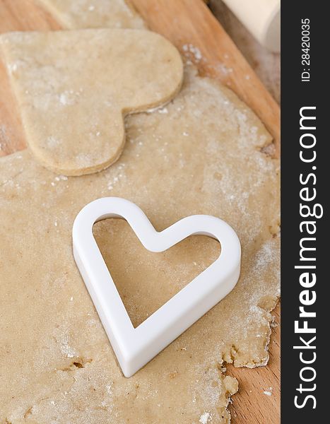 Cookie cutters in the form of heart in cookie dough on a wooden cutting board