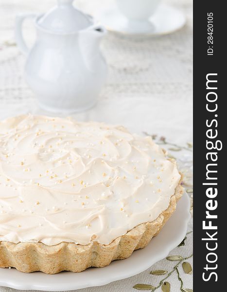 Lemon tart with meringue on a white plate. Teapot and cup in the background. Lemon tart with meringue on a white plate. Teapot and cup in the background.