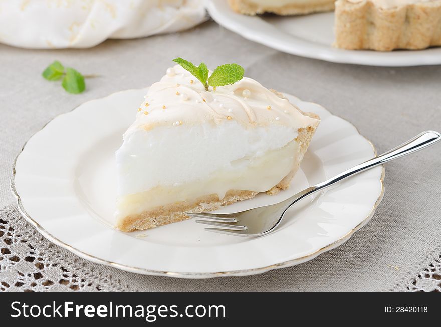 Piece of lemon tart with meringue decorated with fresh mint on a plate closeup