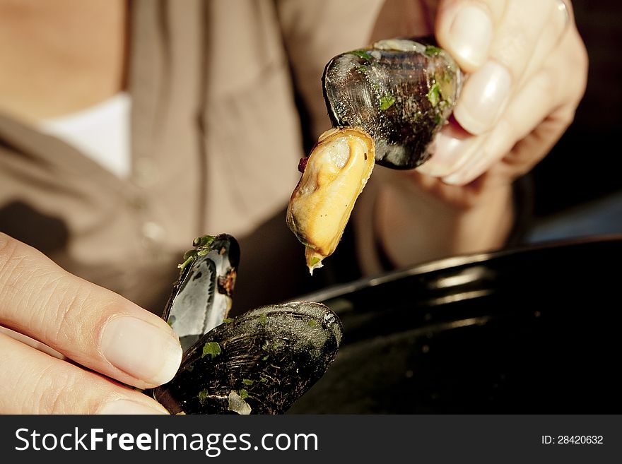 Woman taking a mussel out of a shell. The scene is situated in a warm late afternoon sunlight. She is eating out of a pan which is partially visible. Woman taking a mussel out of a shell. The scene is situated in a warm late afternoon sunlight. She is eating out of a pan which is partially visible.