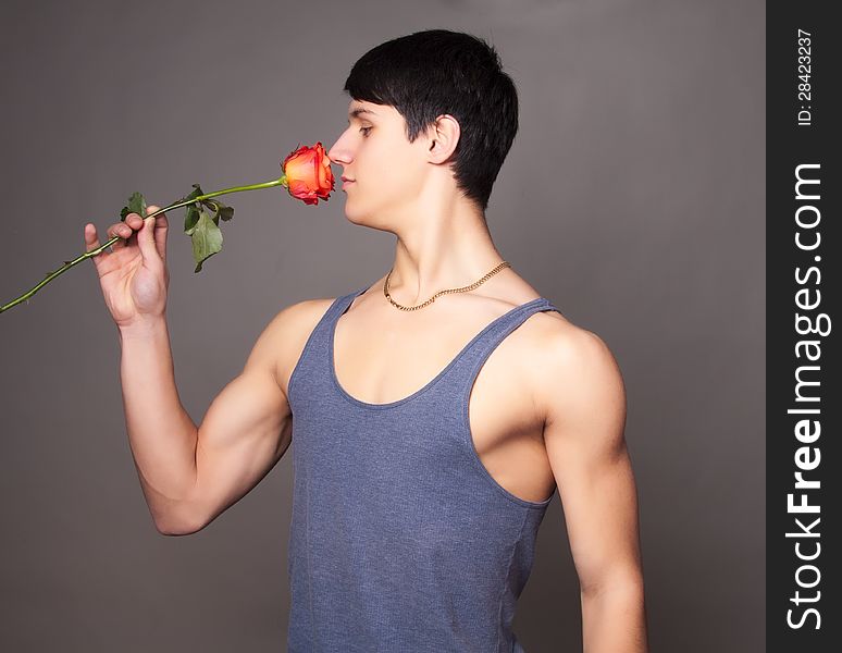 Muscular man with red  rose in hands on gray. Muscular man with red  rose in hands on gray