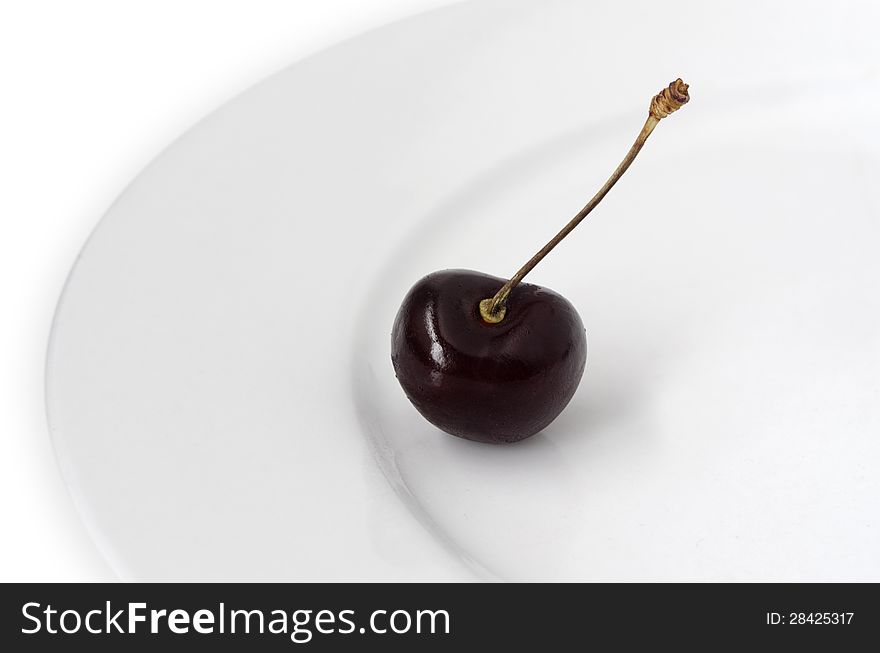 One cherry on a white plate on a white background.