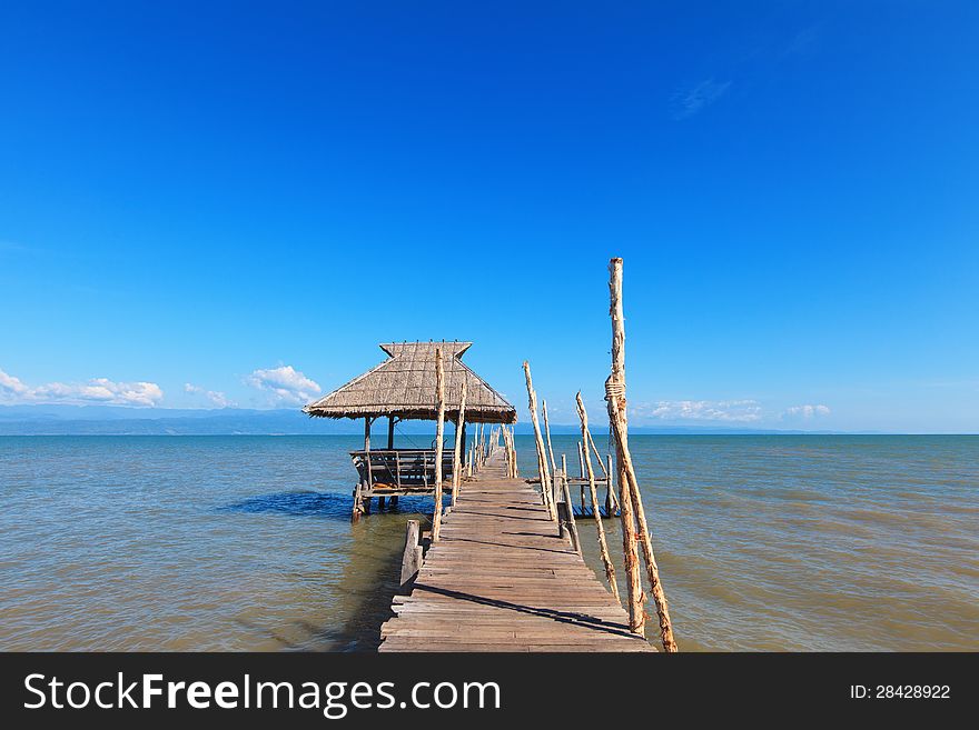 Old wooden boat dock, going far out to sea. Hut with a thatched roof. Blue sky and white clouds. Beautiful sea landscape.