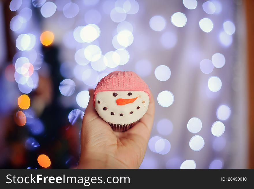 Against abstract sparks of garlands a fruitcake in the form of a snowman. Against abstract sparks of garlands a fruitcake in the form of a snowman