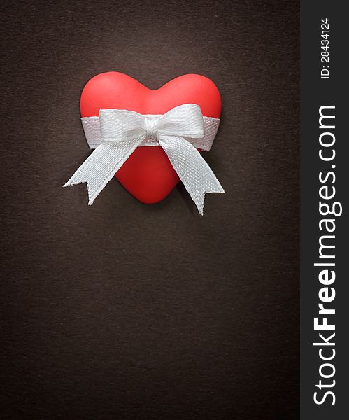 Red heart with a white bow on a background of brown paper. Red heart with a white bow on a background of brown paper