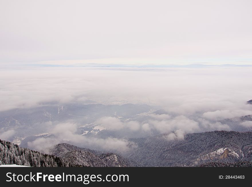 A view from a mountain peak down into a valley with forests and clouds in the sky. A view from a mountain peak down into a valley with forests and clouds in the sky.