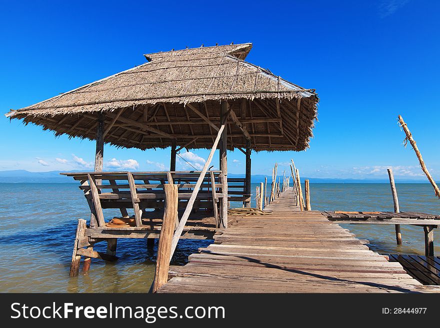 Old wooden boat dock, going far out to sea. Hut with a thatched roof. Blue sky and white clouds. Beautiful sea landscape.