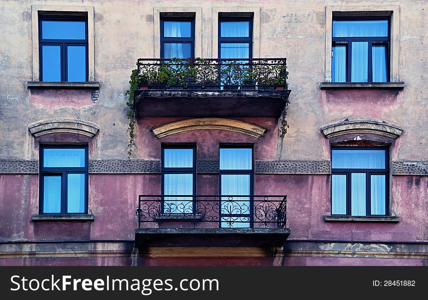 Facade of an old house with metal balconies and overgrown with flowers