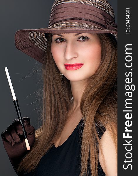 Portrait of a beautiful woman in black dress, brown hat and mouthpiece with cigarette. Portrait of a beautiful woman in black dress, brown hat and mouthpiece with cigarette