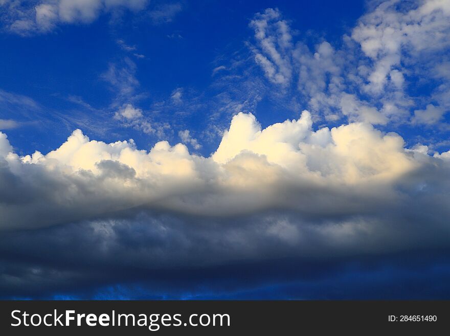 Cumulus large clouds illuminated by the summer sun drift across the blue sky.