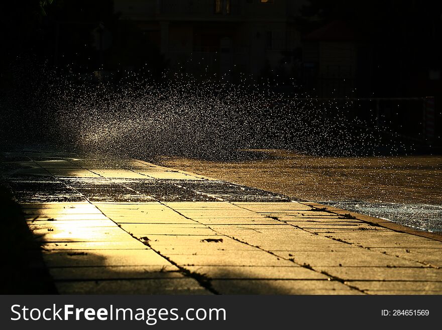 Water droplets over the granite path, illuminated by the morning sun, scatter to the sides against a dark background.