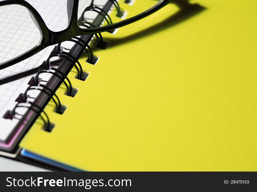 Closeup of black spectacles lying on spiral notebook. Good background for text. Closeup of black spectacles lying on spiral notebook. Good background for text