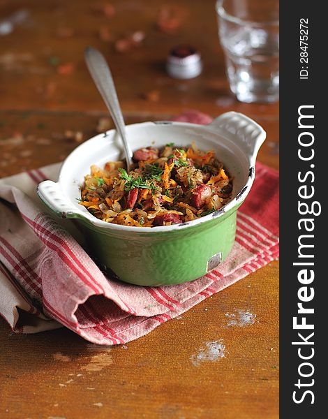 Stewed cabbage with sausages, carrots and lentil in a green sauce pan on a kitchen towel. Stewed cabbage with sausages, carrots and lentil in a green sauce pan on a kitchen towel