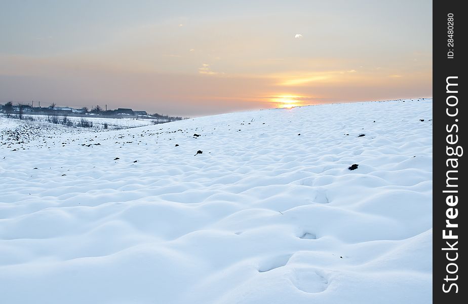 Snowy field at sunset with distant houses. Snowy field at sunset with distant houses