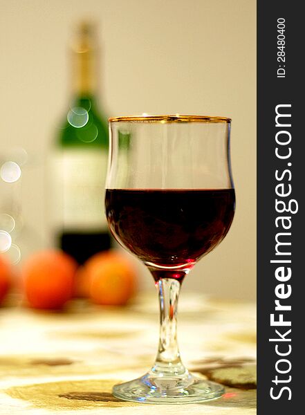 Wine glass on a table with bottle and oranges behind it.