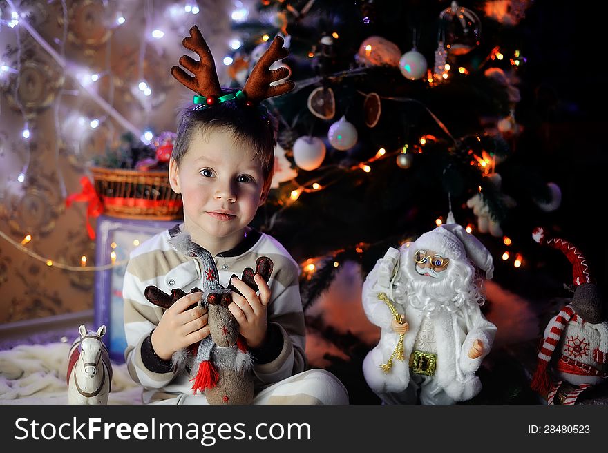 The boy sits with beautiful toys under a fur-tree with small horns on a head. The boy sits with beautiful toys under a fur-tree with small horns on a head