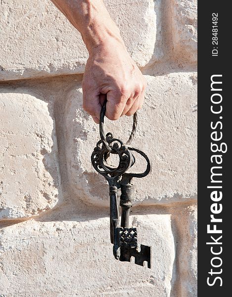 Hand holding vintage keys against a wall lined with white stones of the great. Hand holding vintage keys against a wall lined with white stones of the great