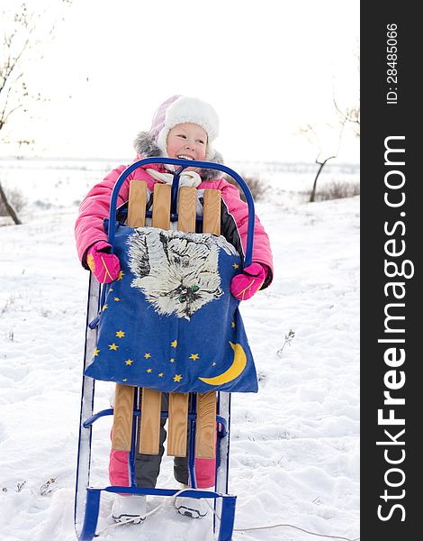 Merry little girl holding her winter sled up in front of her laughing and looking out of the frame