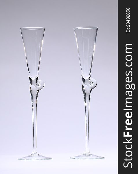 TWo Champagne glasses, lit partly from behind, empty in front of neutral, light grey background. TWo Champagne glasses, lit partly from behind, empty in front of neutral, light grey background