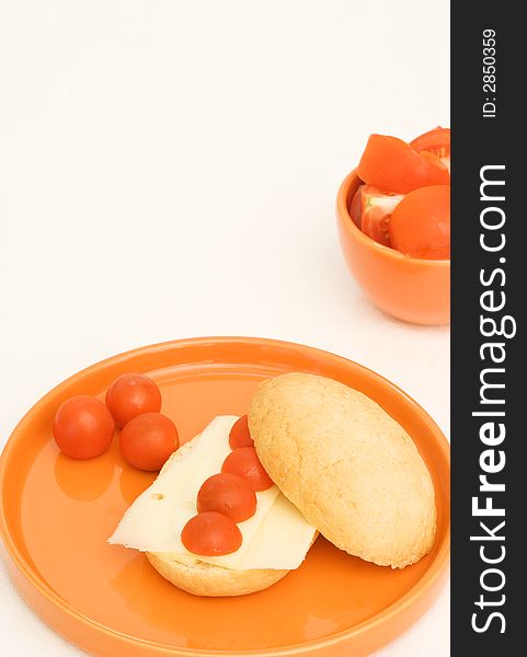 Tomato and cheese breakfast bun on orange plate. Tomato and cheese breakfast bun on orange plate