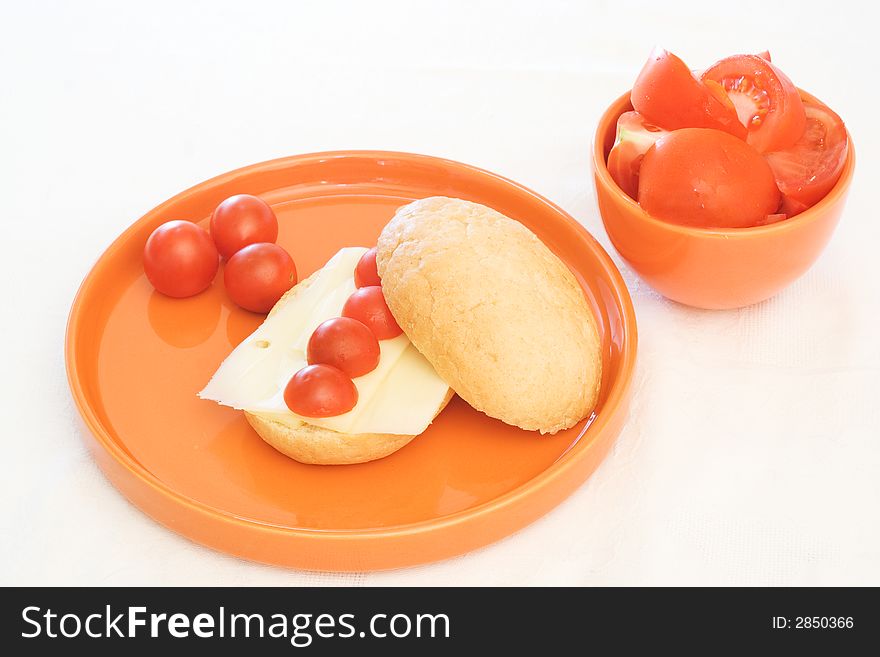 Tomato and cheese breakfast bun on orange plate. Tomato and cheese breakfast bun on orange plate