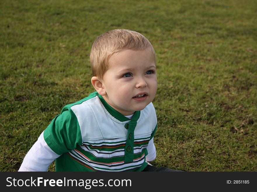 Young boy looking up into the distance, sitting on the grass