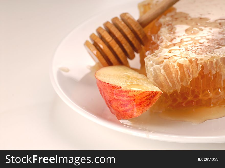 A honeycomb, honey wand and apple on a plate. A honeycomb, honey wand and apple on a plate