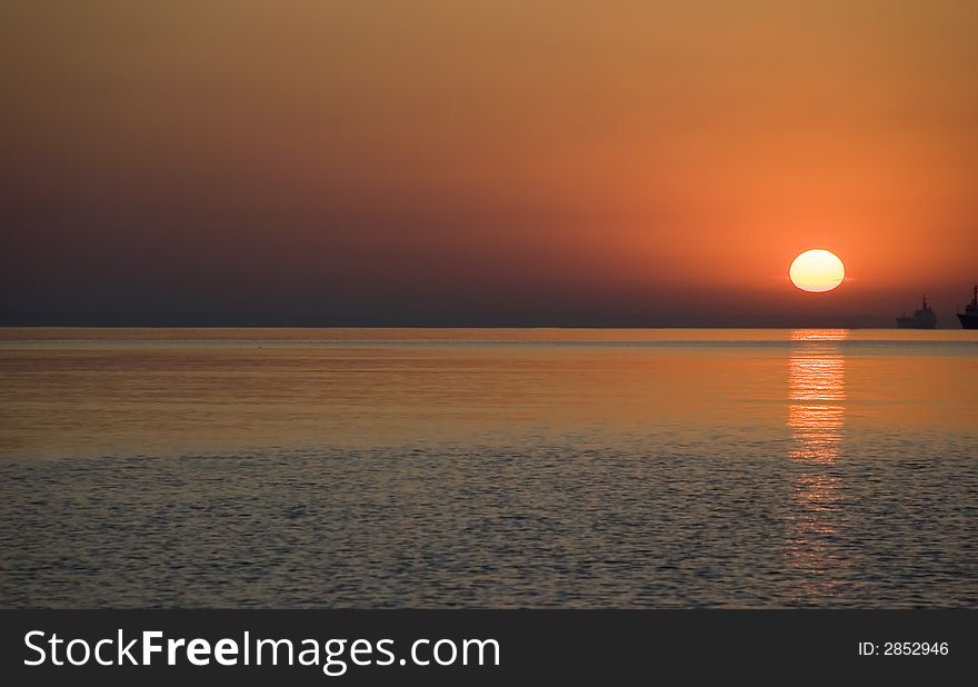 Red sunrise above ocean. With the military ships on a background