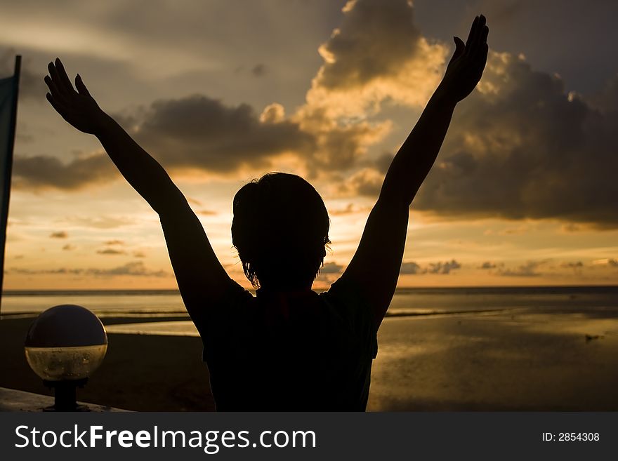 A silhouette of a girls with arms raised during sunset. A silhouette of a girls with arms raised during sunset