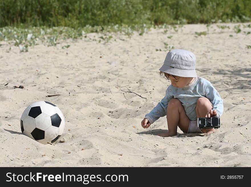 The boy plays on sand with the toy automobile near to a football. The boy plays on sand with the toy automobile near to a football