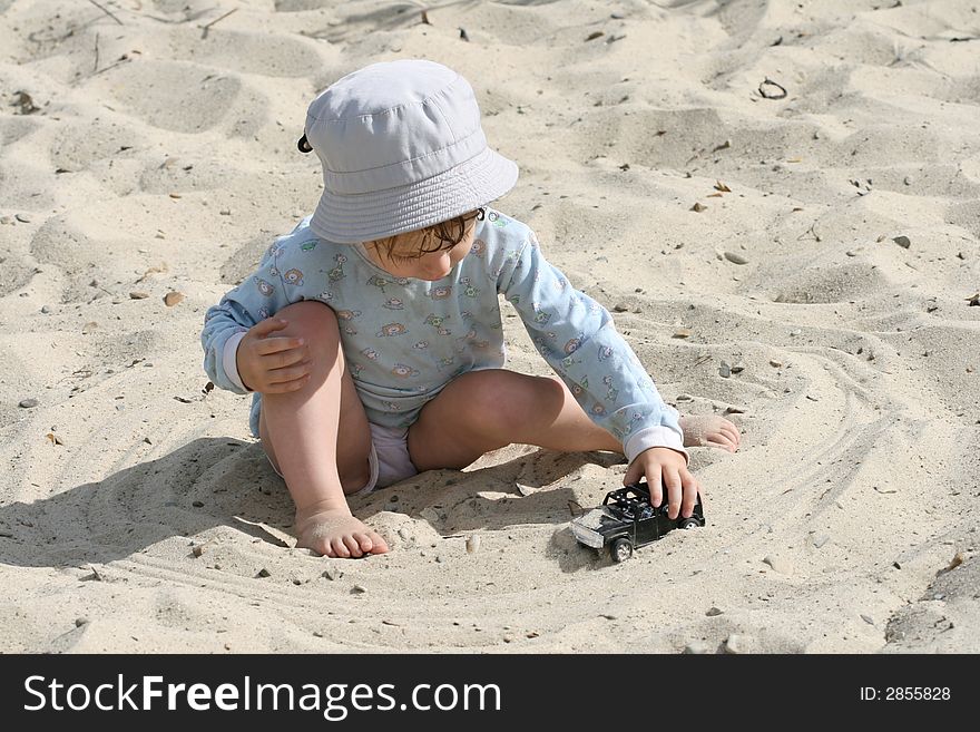 The boy on sand plays with the toy automobile