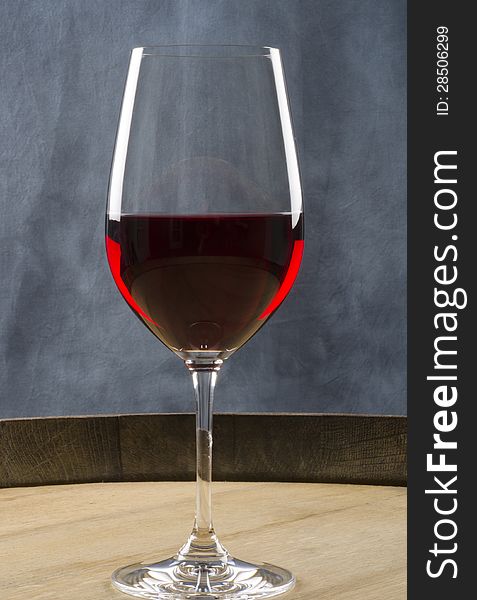 A glass of red wine on top of a wine barrel.