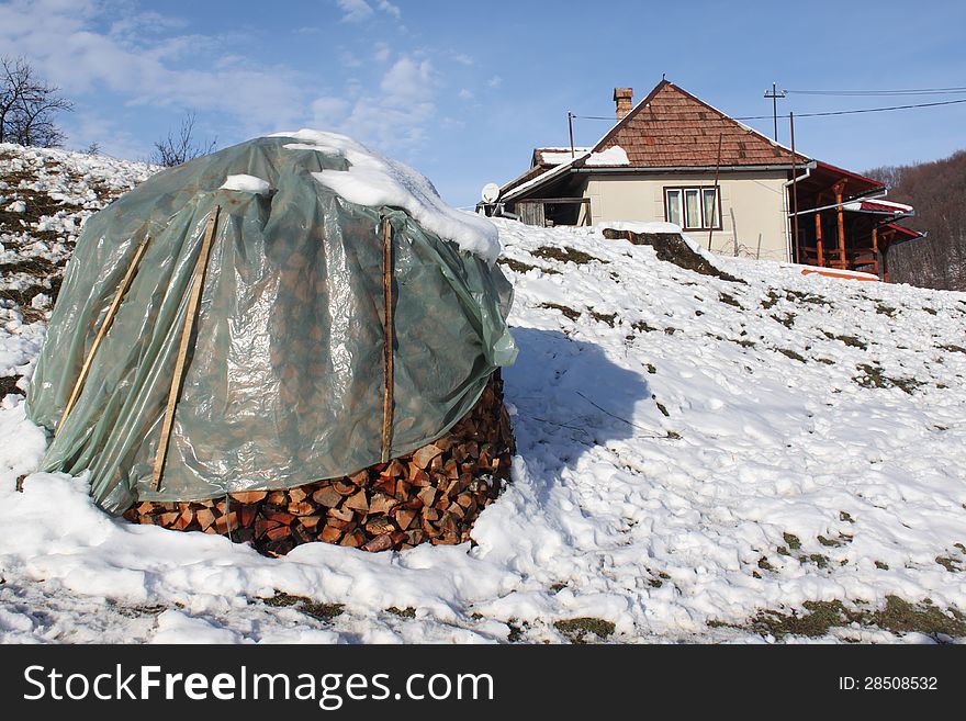 Pile of wood for winter covered with plastic near house