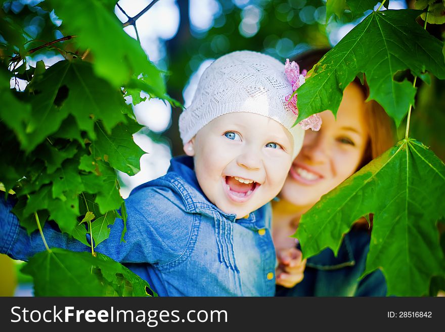 Little laughing girl looking through leaves of a tree, she is happy. Little laughing girl looking through leaves of a tree, she is happy