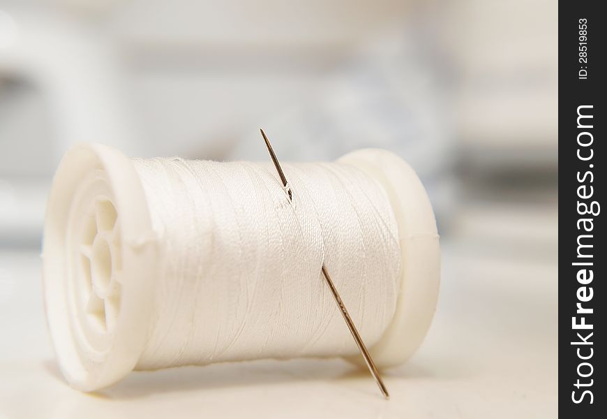 White thread on spool, laying down, with a needle