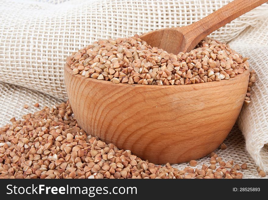 Raw buckwheat in wooden bowl and spoon on burlap, food ingredient photo